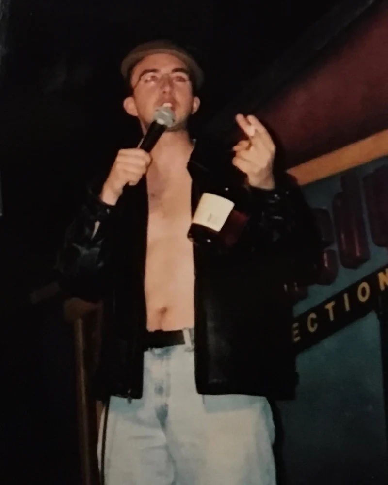 Comedian Joe List of Tuesdays with Stories performing stand-up comedy in a leather jacket with a bottle of cognac in his hand. Find more about Joe at www.tuesdayspod.com/joe-list