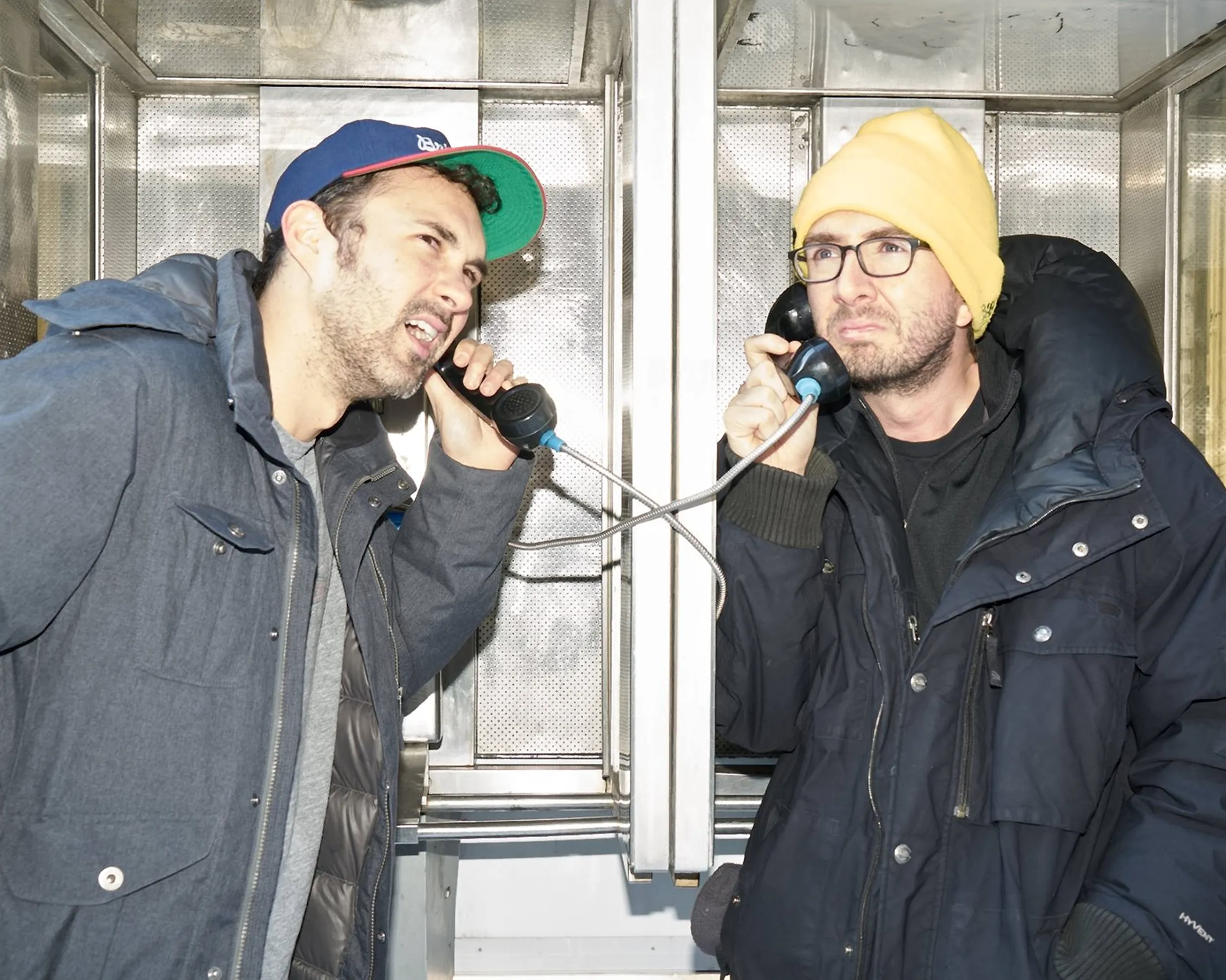 Comedians Mark Normand and Joe List of Tuesdays with Stories calling each other at a double telephone booth. Find Mark Normand Tour Dates and Joe List Tour Dates at www.tuesdayspod.com/find-a-show