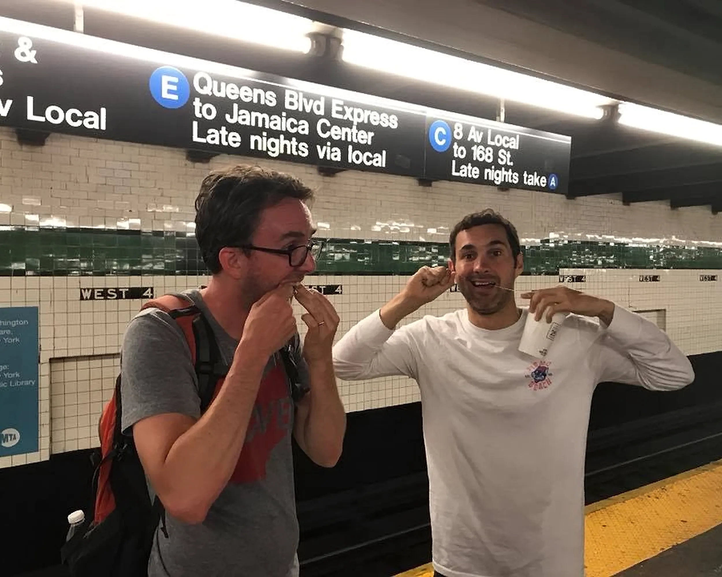 Comedians Mark Normand and Joe List of Tuesdays with Stories, flossing with dental floss, at the West Fourth Street–Washington Square Subway Train Station.. Find Mark Normand Tour Dates and Joe List Tour Dates at www.tuesdayspod.com/find-a-show